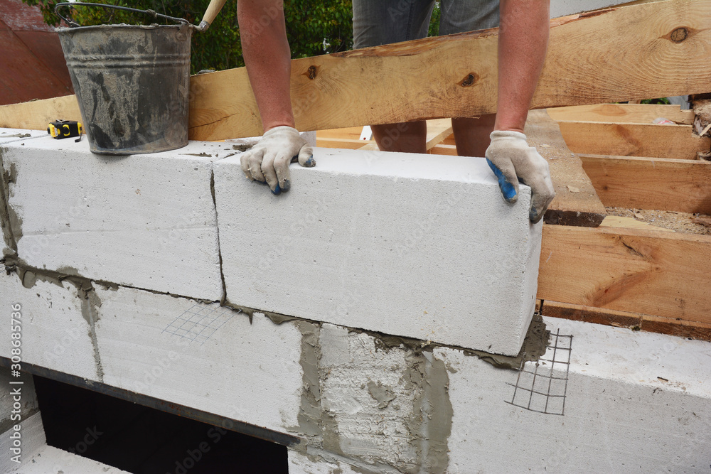 Bricklayer builder laying autoclaved aerated concrete blocks, aac for new house wall.