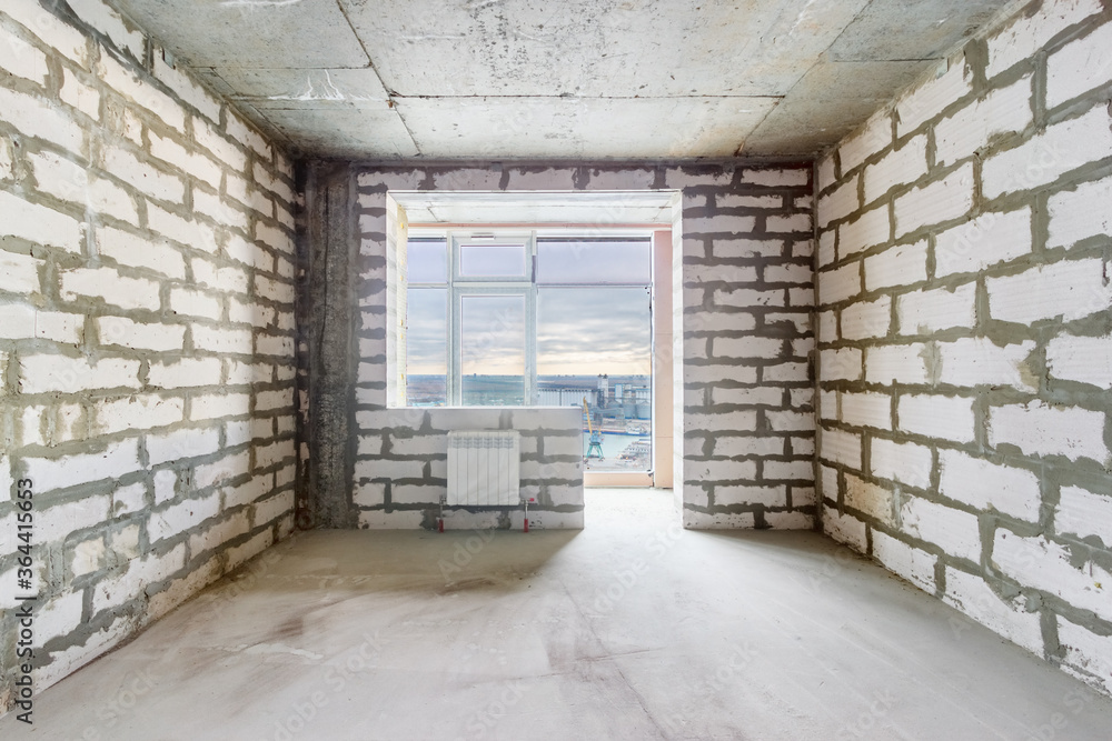The unfinished room in a residential building under construction with the window, the balcony and the bare walls. The use of aerated concrete blocks in high-rise building construction