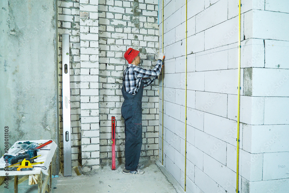man in work wear installing metal rails onto aerated concrete block wall for home construction